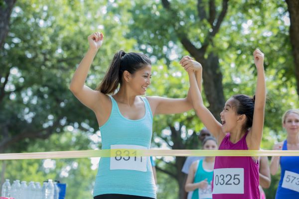 A woman and a young girl in running gear about to cross the finish line ribbon.