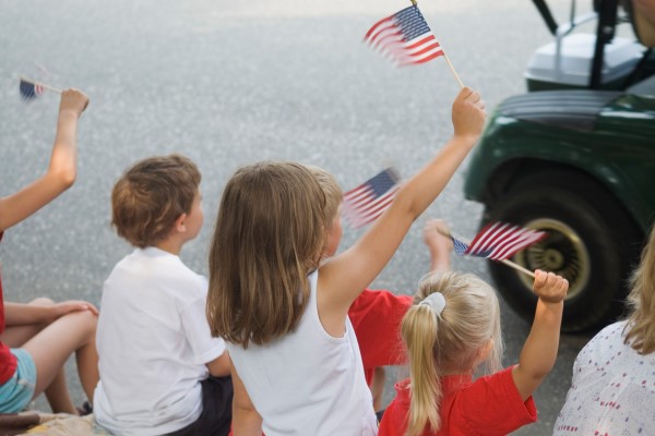 Children waiving American flags along a parade route.