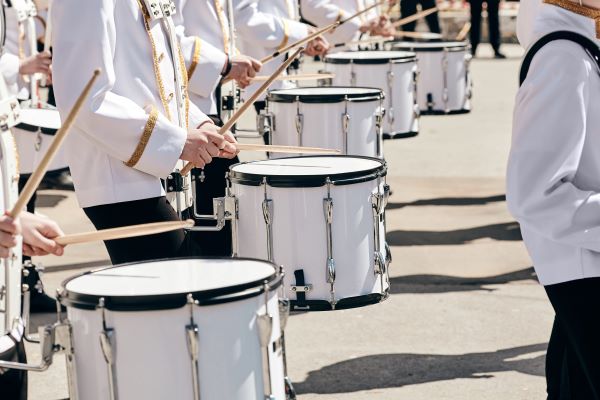 A line of drummers in white uniforms with white drums in a marching line.