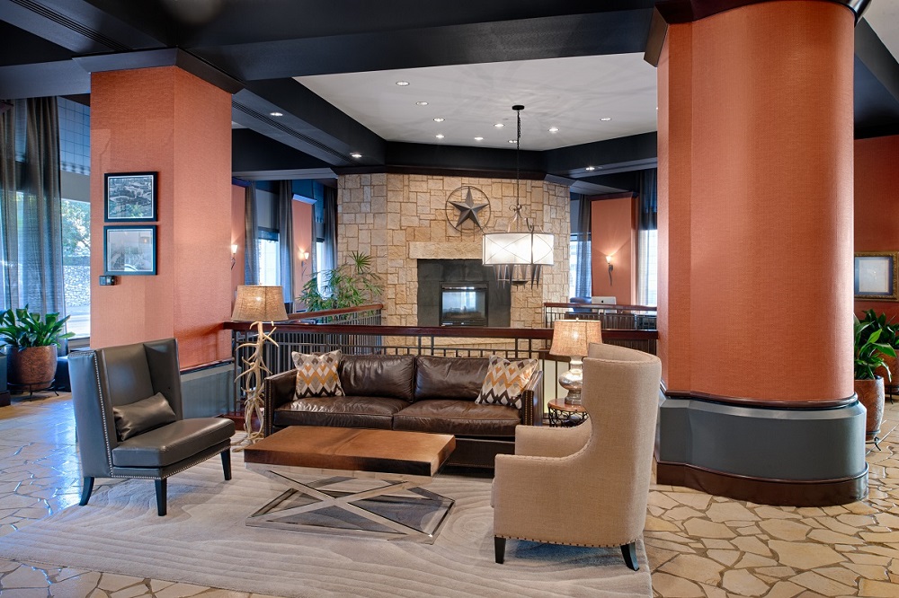 The lobby of the Emily Morgan hotel, with a fireplace, a sofa, and lounge chairs.