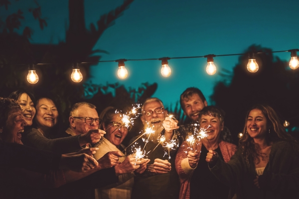 Nine people holding sparklers together beneath a string of lights at night.
