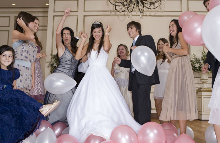 A girl in a white dress amidst balloons celebrating her quincenera with family and friends.