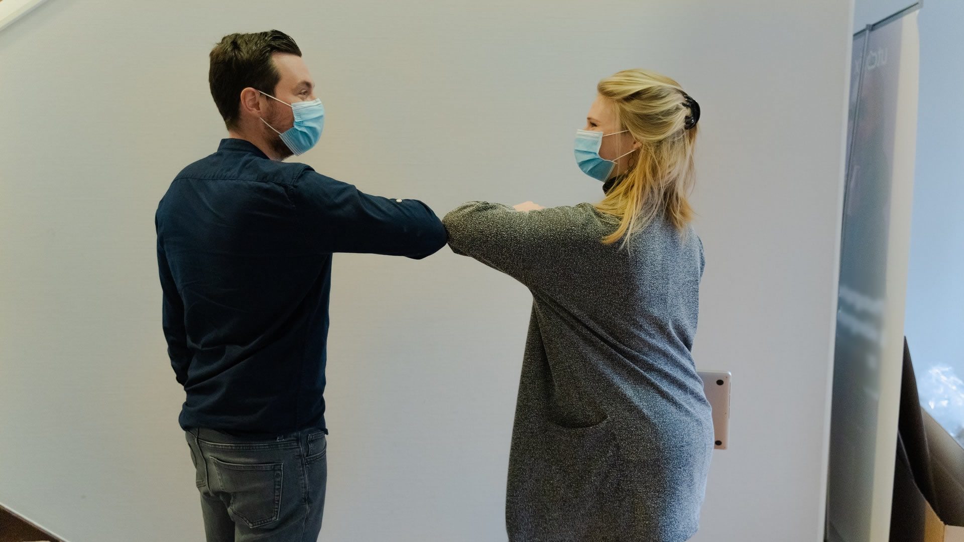 A man and a woman doing an elbow bump while wearing face masks.