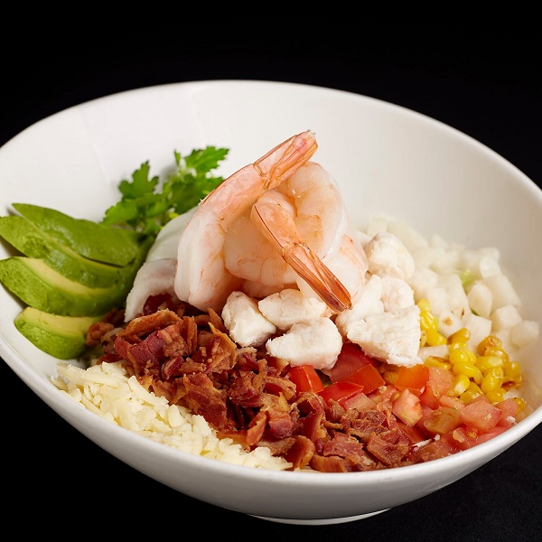 A bowl with shrimp, avocado, bacon, corn, and other healthy ingredients.