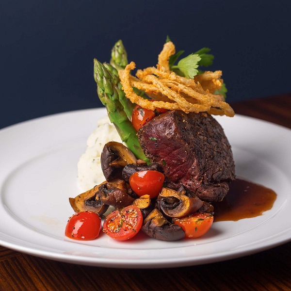 A steak entree with mashed potatoes, asparagus, and tomatoes.