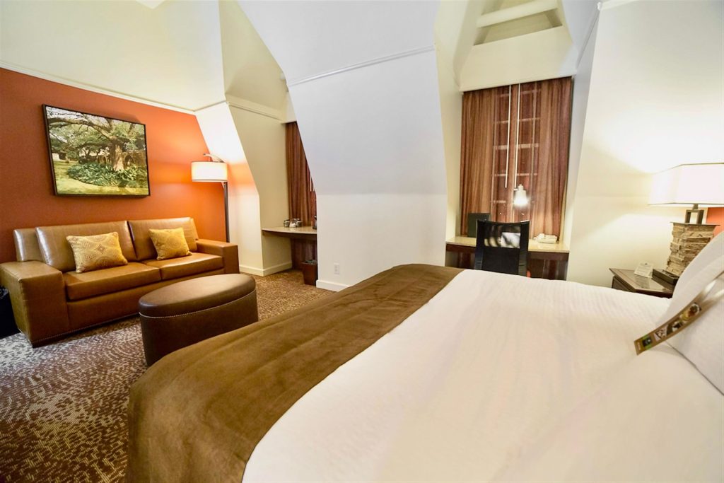 A guestroom at Emily Morgan Hotel featuring a king bed, sleeper sofa, executive work desk, and views of San Antonio.
