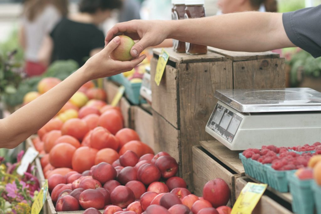 Man handing an apple to a customer at a farmer's market.