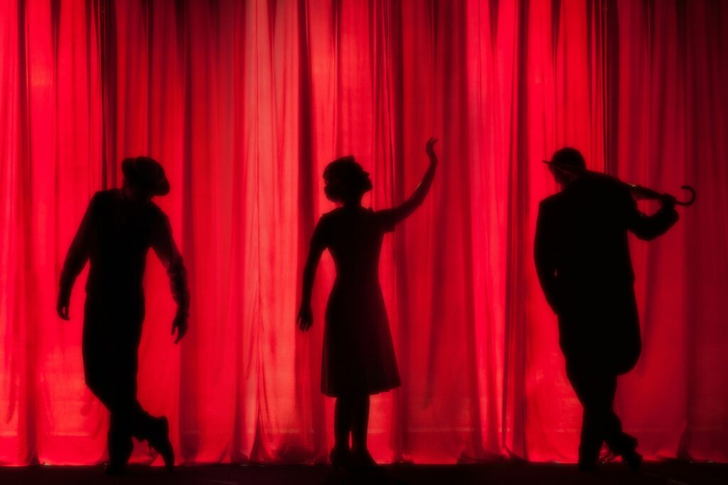Silhouettes of actors in front of a red theater curtain.