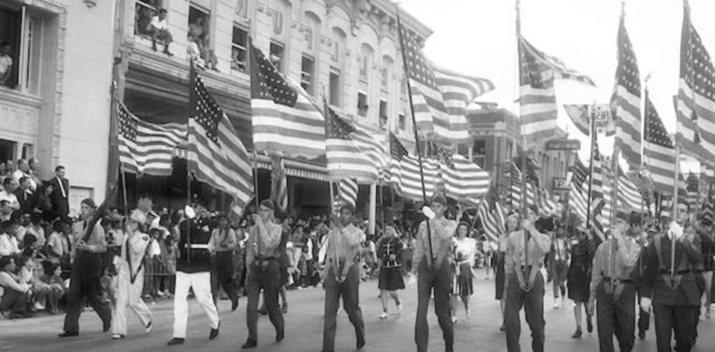 Historic photo of a parade in San Antonio with men carrying American flags.