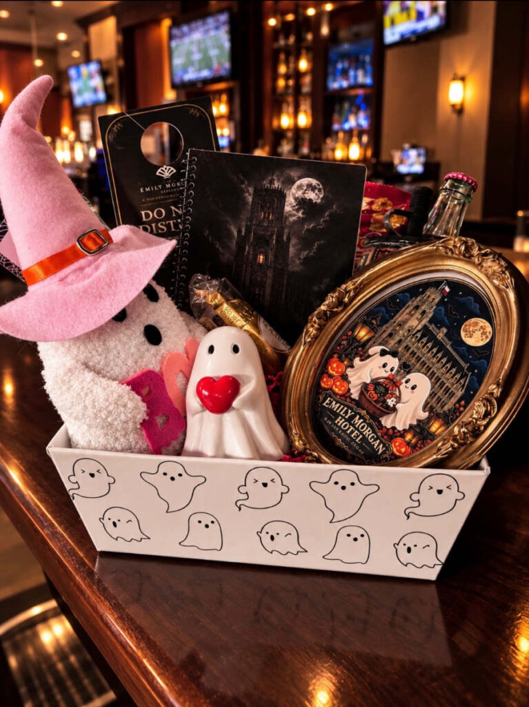 Emily Morgan Hotel Halloween gift basket featuring ghost-themed keepsakes, a plush ghost in a pink witch hat, decorative ghost, Haunted Emily Morgan Book, framed hotel artwork, and seasonal treats.